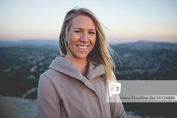 Portrait of smiling woman standing on mountain against sky during sunset