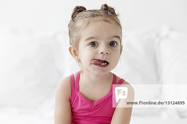 Porträt eines Mädchens mit Zunge  das zu Hause auf dem Bett sitzt