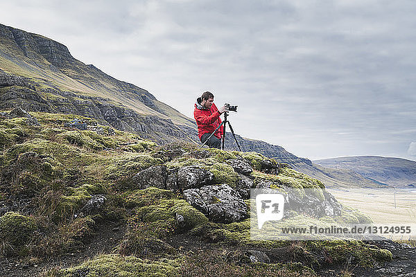 Mann fotografiert  während er auf einem Hügel vor bewölktem Himmel steht