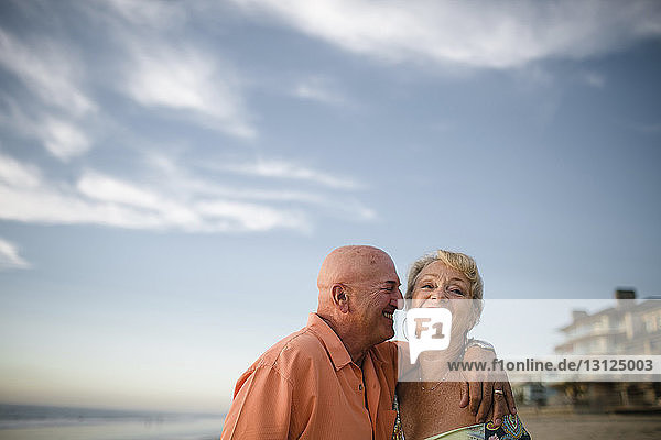 Lächelndes älteres Paar  das bei Sonnenuntergang am Strand gegen den Himmel steht