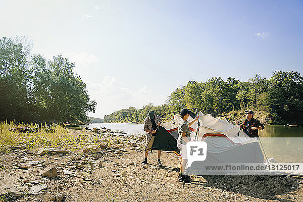 Männliche Freunde versammeln Zelt auf einem Campingplatz am See gegen den Himmel