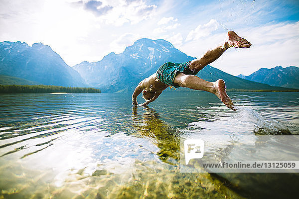 Man diving into lake against mountains and sky