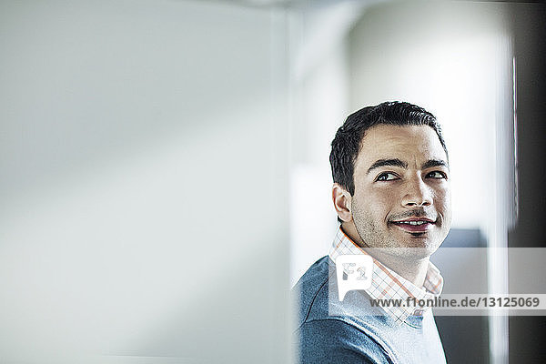 Smiling thoughtful businessman leaning against wall in office
