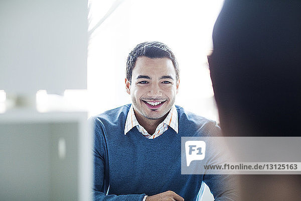 Selbstbewusst lächelnder Geschäftsmann sitzt am Bürotisch gegen das Fenster