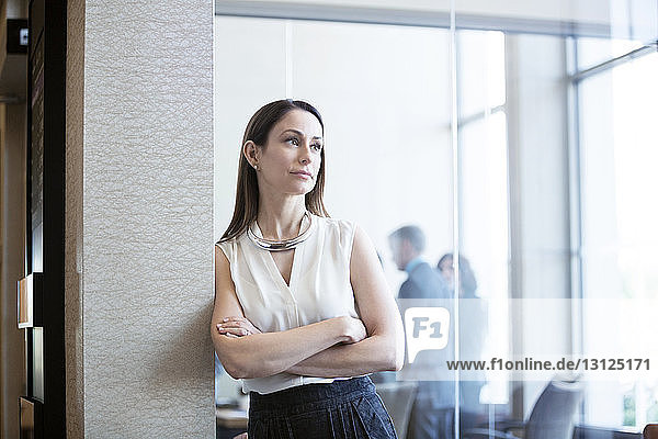 Thoughtful businesswoman leaning on wall in office