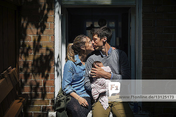 Paar mit küssendem Baby  das an der Tür sitzt