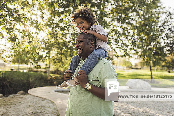 Fröhlicher Vater trägt Sohn auf den Schultern im Park