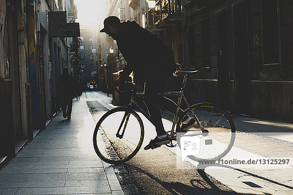 Seitenansicht eines Mannes  der bei Sonnenuntergang auf einem Fußweg Fahrrad fährt