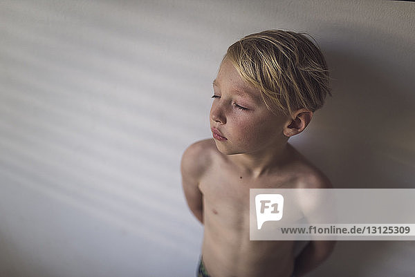 Hochwinkelaufnahme eines Jungen ohne Hemd  der zu Hause an der Wand steht