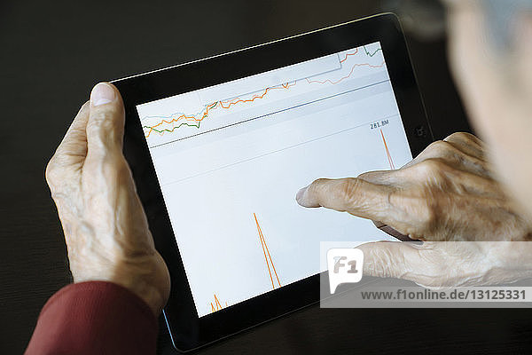 Ausgeschnittenes Bild eines leitenden Angestellten  der eine Grafik auf einem Tablet-Computer im Büro eines Finanzberaters analysiert