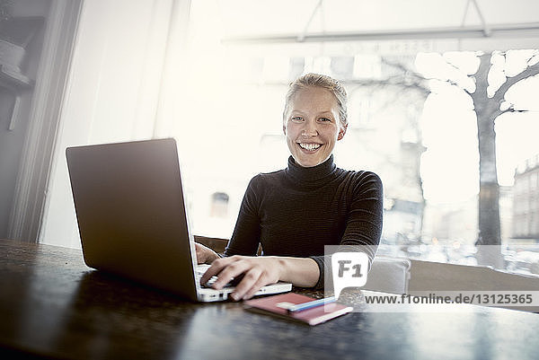 Portrait of happy young woman with laptop at cafe table