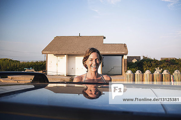 Glückliche Frau steht hinter Auto gegen Haus