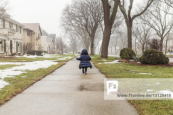 Rückansicht eines Mädchens mit Kapuzenjacke beim Laufen auf einem Fußweg im Winter