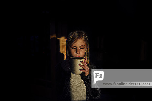 Mädchen mit geschlossenen Augen hält Becher  während sie zu Hause in der Dunkelkammer steht