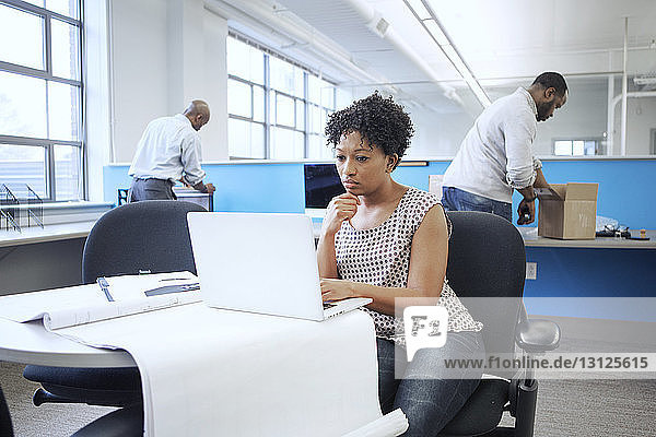 Businesswoman using laptop computer while male colleagues working in background