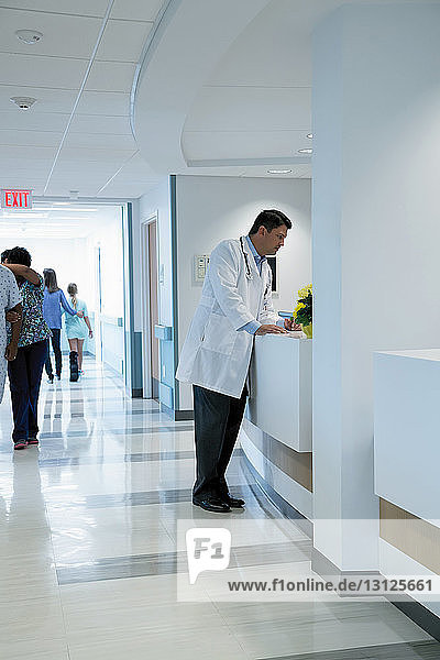 Doctor standing at hospital reception with colleagues and patients in background
