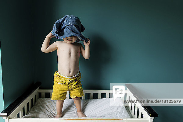 Junge zieht Hemd aus  während er im Etagenbett an der Wand steht