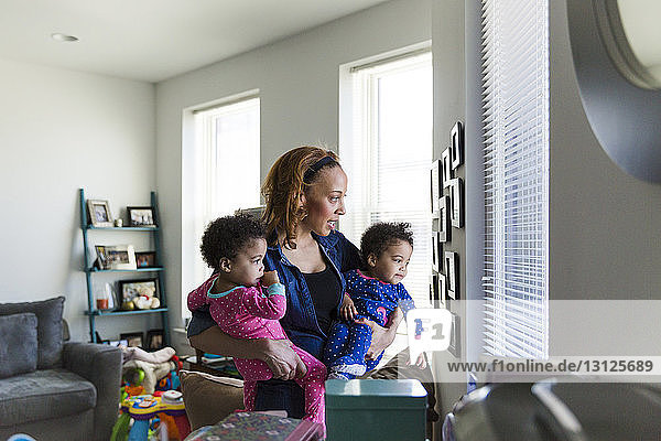 Mother and daughters looking through window blinds at home