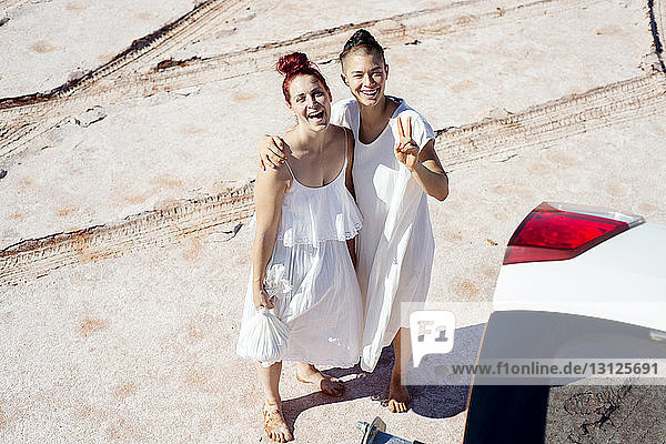 Hochwinkel-Portraitaufnahme von glücklichen Freundinnen  die am Strand stehen