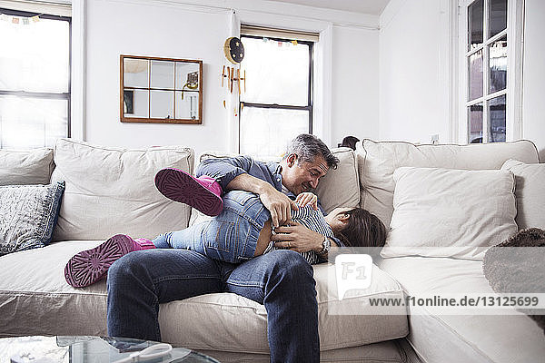 Cheerful Father playing with daughter on sofa at home