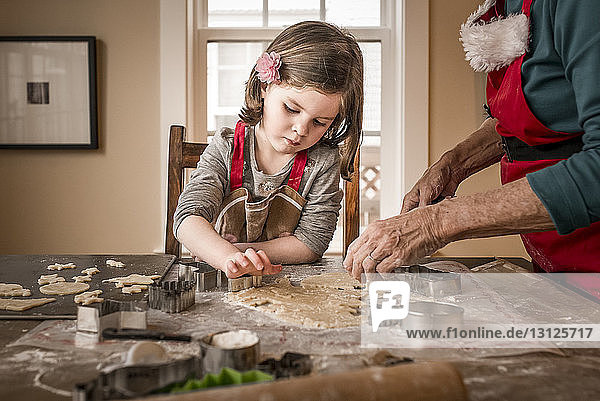 Granddaughter helping grandmother in making Christmas cookies on table at home