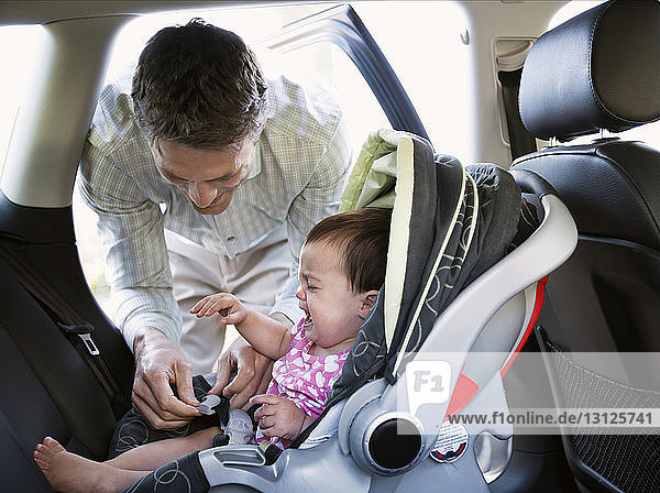 Baby weint  während der lächelnde Vater den Autositz verriegelt
