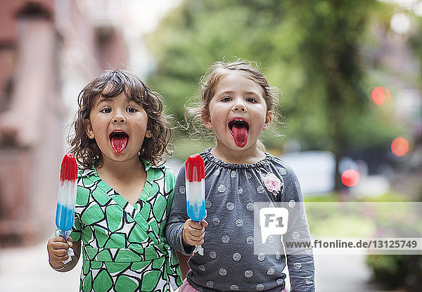 Portrait of girls sticking out tongue while holding ice lollies