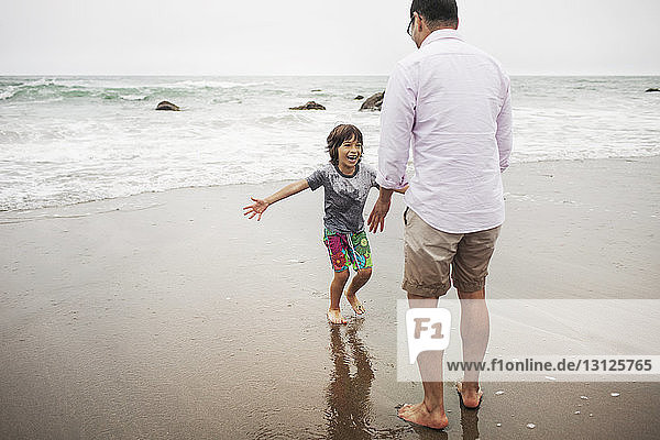 Vater und Sohn spielen auf nassem Sand am Ufer