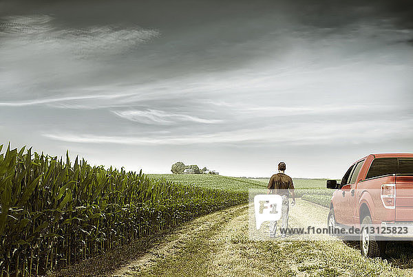 Rear view of farmer standing by car on field against cloudy sky
