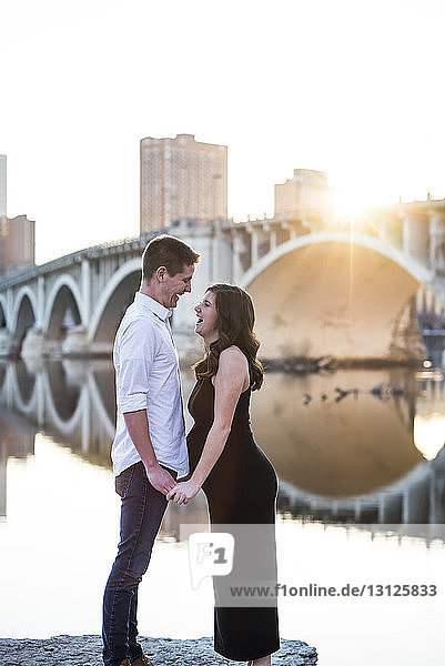Happy couple holding hands while standing by river against clear sky in city