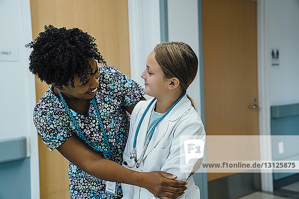 Kinderarzt umarmt Mädchen  während er im Krankenhauskorridor steht