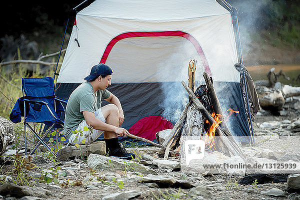 Side view of young man sitting at campsite during sunset
