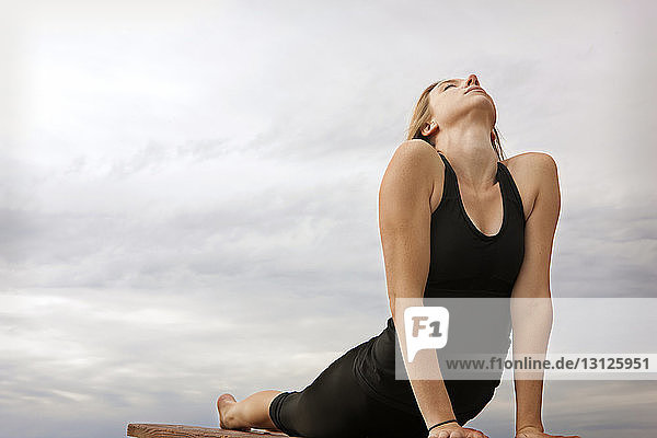 Junge Frau übt Yoga mit nach oben gerichteter Hundehaltung bei bewölktem Himmel