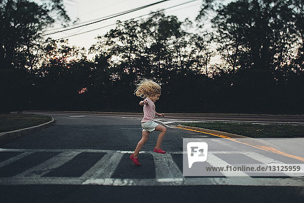 Side view of girl jumping on zebra crossing against trees