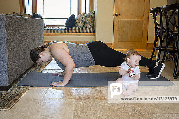 Mother practicing push-ups while cute son playing with toy at home
