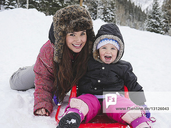 Portrait of happy mother with daughter sitting on snow covered field