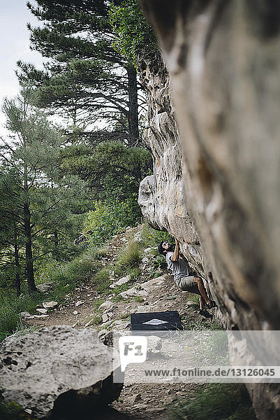 Wanderer klettert an einer Felsformation bei Bäumen im Wald