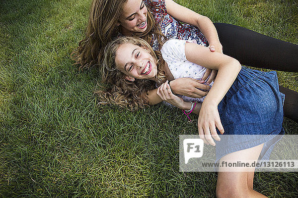 Mother and daughter enjoying while lying on grassy field at park