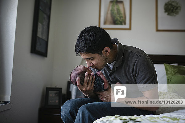 Vater spielt mit neugeborenem Sohn  während er zu Hause auf dem Bett sitzt