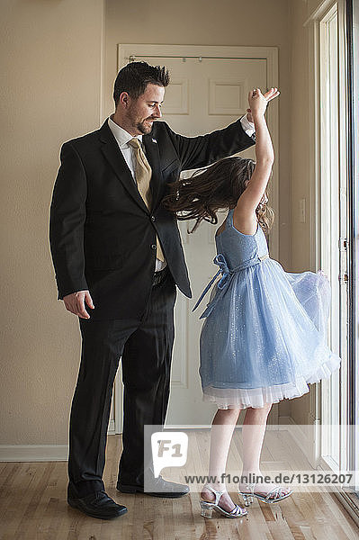 Tochter dreht sich  während sie zu Hause mit dem Vater auf dem Holzboden tanzt