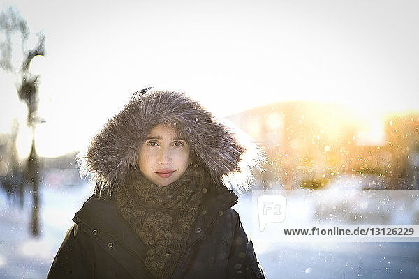 Portrait of woman wearing fur hood standing in city during winter