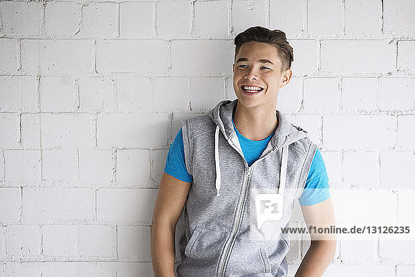 Cheerful male athlete standing against brick wall