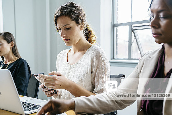 Geschäftsfrau benutzt Smartphone  während sie mit Kollegen im Büro sitzt