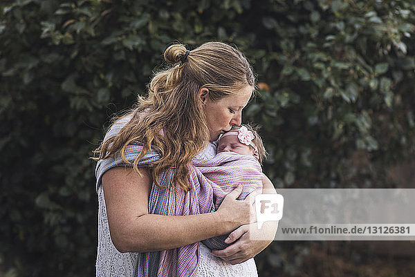 Mutter küsst neugeborene Tochter  während sie im Hinterhof steht