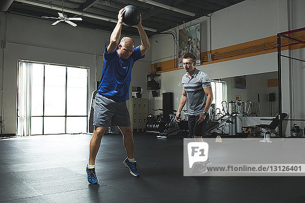 Trainer looking at customer exercising with fitness ball in gym