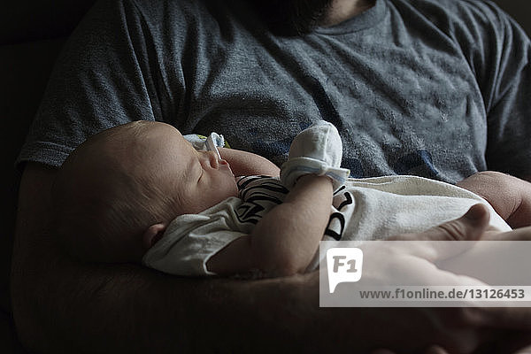 Midsection of father carrying sleeping newborn son at home