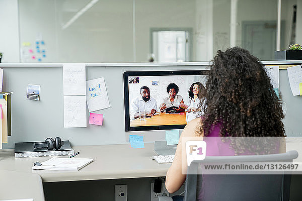 Rückansicht der Videokonferenz einer Geschäftsfrau mit ihren Kollegen über einen Desktop-Computer am Schreibtisch im Büro