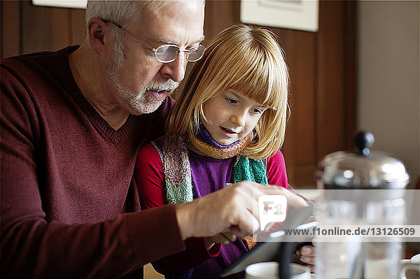 Großvater zeigt der Enkelin einen Tablet-Computer  während er am Tisch sitzt