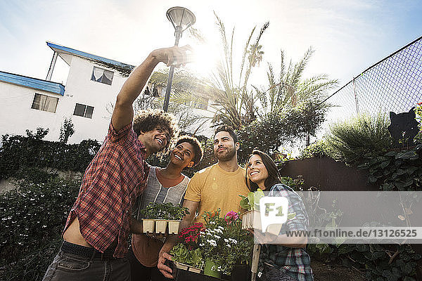 Happy multi-ethnic friends taking selfie while holding potted plants in community garden