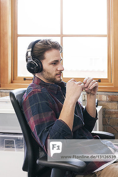 Seitenansicht eines auf einem Bürostuhl sitzenden Geschäftsmannes mit Kopfhörern